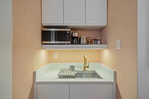 Una cocina compacta con microondas, cafetera y una repisa con diversos objetos.