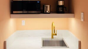 Una cocina compacta con microondas integrado, cafetera y lavamanos con grifo dorado.