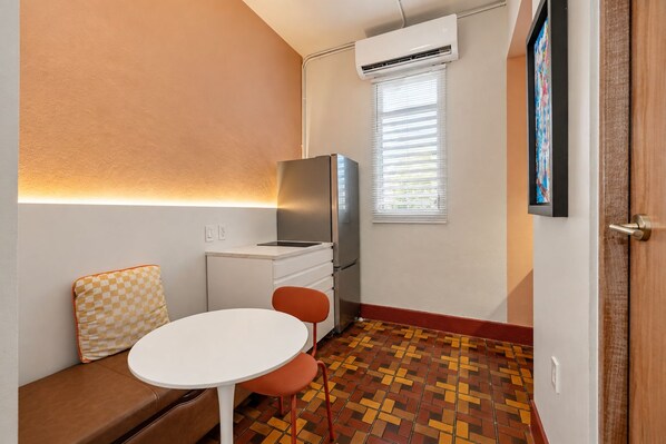A compact room with a kitchenette, a dining area with a table and chairs, a bench, a patterned floor, and a door. - Cozy Apartment near Ocean Park San Juan! (San Juan)