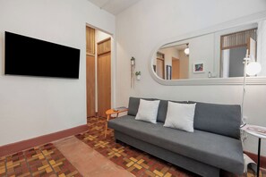 Una sala de estar moderna con un sofá gris, un televisor de pantalla plana, una mesita auxiliar, una alfombra estampada y un espejo.
