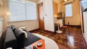 Habitación de hotel compacta con sofá, una mesita, una silla y una kitchenette.