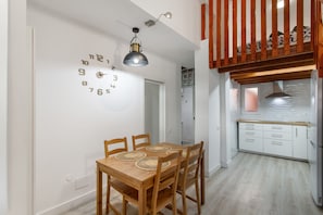 Un comedor con una mesa y sillas de madera, un reloj de pared y una cocina al fondo.