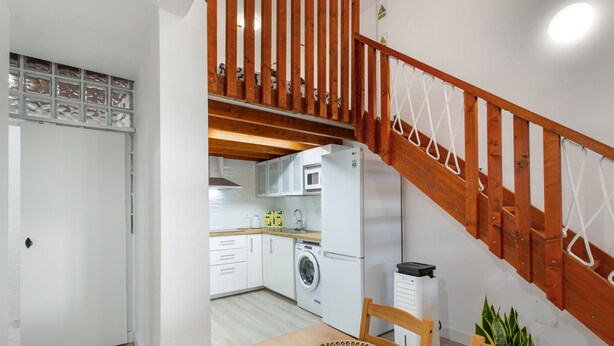 A modern kitchen with white cabinets, a washing machine, and a dining area with a wooden table and chairs.