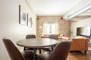 Un soggiorno moderno con parete in mattoni, un tavolo da pranzo rotondo con sedie, un divano e una TV a schermo piatto.