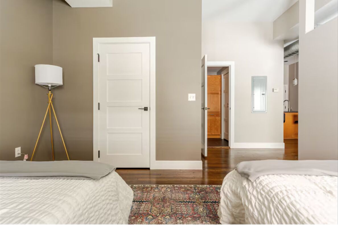 Une chambre avec deux lits, une lampe et une porte donnant sur un couloir.