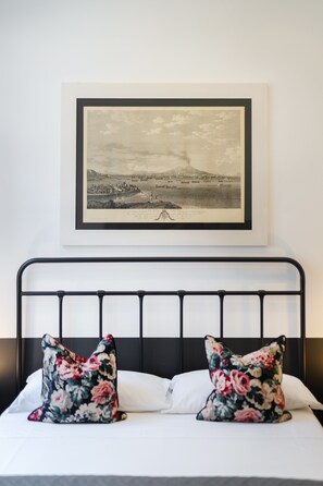 A neatly made bed with a black metal frame, two floral pillows, and a framed black and white landscape picture above it. - SALOTTO BORBONICO - SANFELICE (Naples)