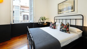 A bedroom with a bed, a nightstand, a window with a view of buildings, and a framed picture on the wall. - SALOTTO BORBONICO - SANFELICE (Naples)