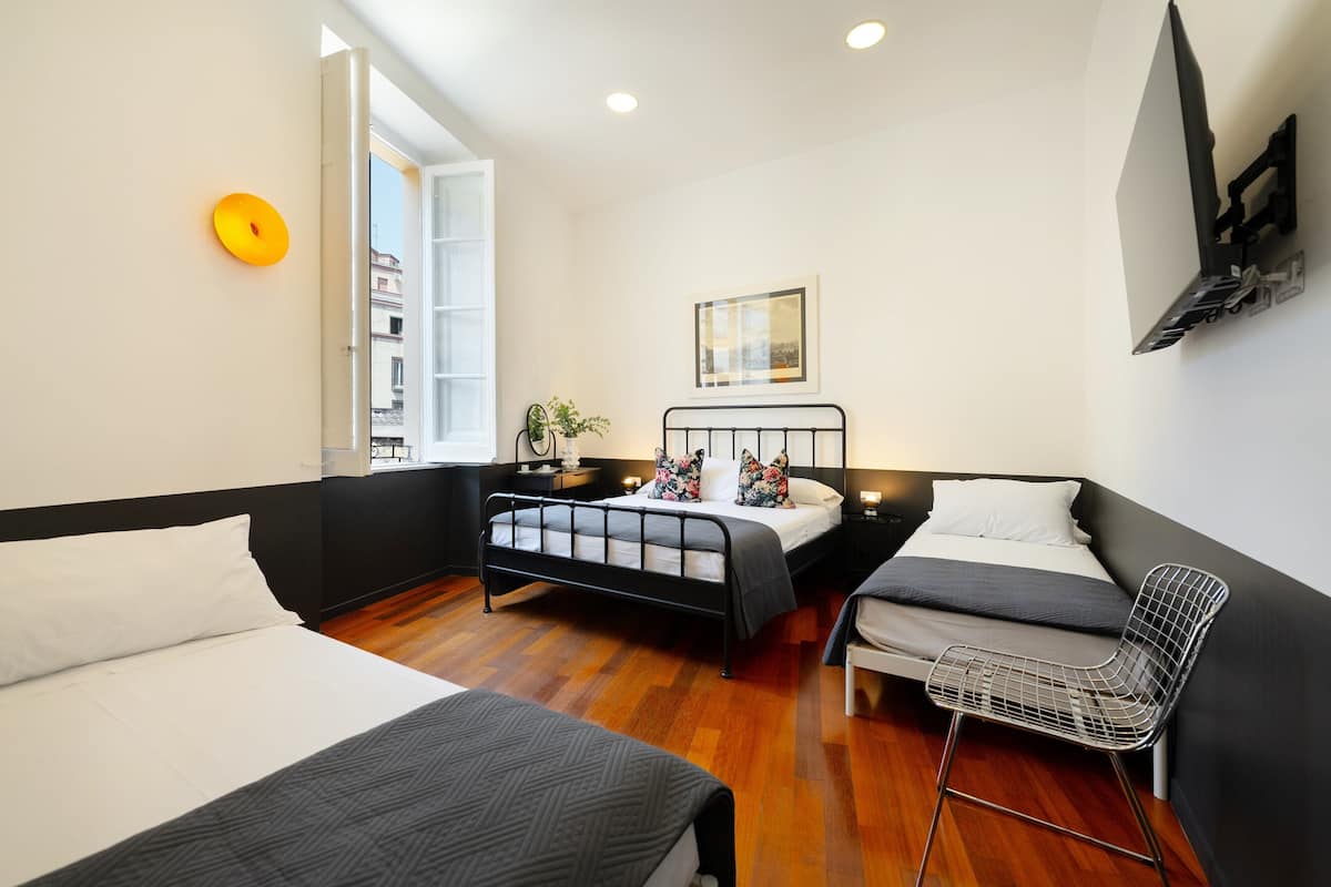 A modern bedroom with two beds, a chair, a window, and a wall-mounted TV.