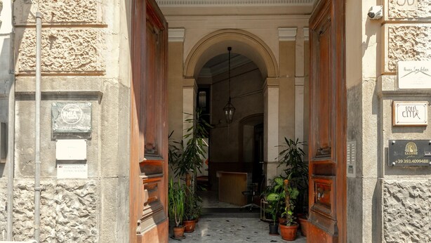A stone building entrance with a decorative archway, potted plants, and a sign indicating the address. - SALOTTO BORBONICO - SANFELICE (Naples)