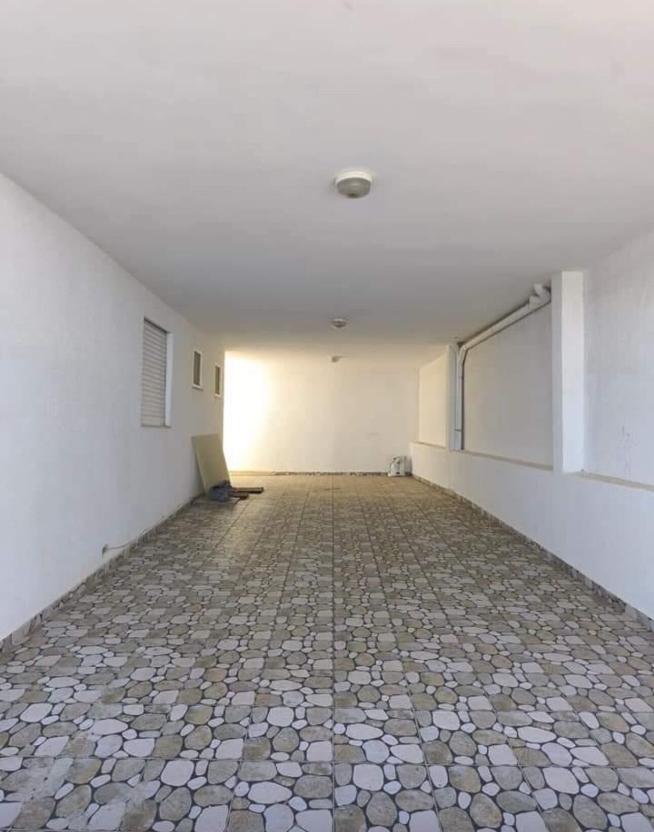 Un pasillo con piso de baldosas, paredes blancas y una lámpara en el techo.