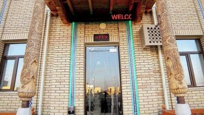 A hotel entrance with a wooden canopy, a 'Welcome' sign, and a 'Open' sign above the door.