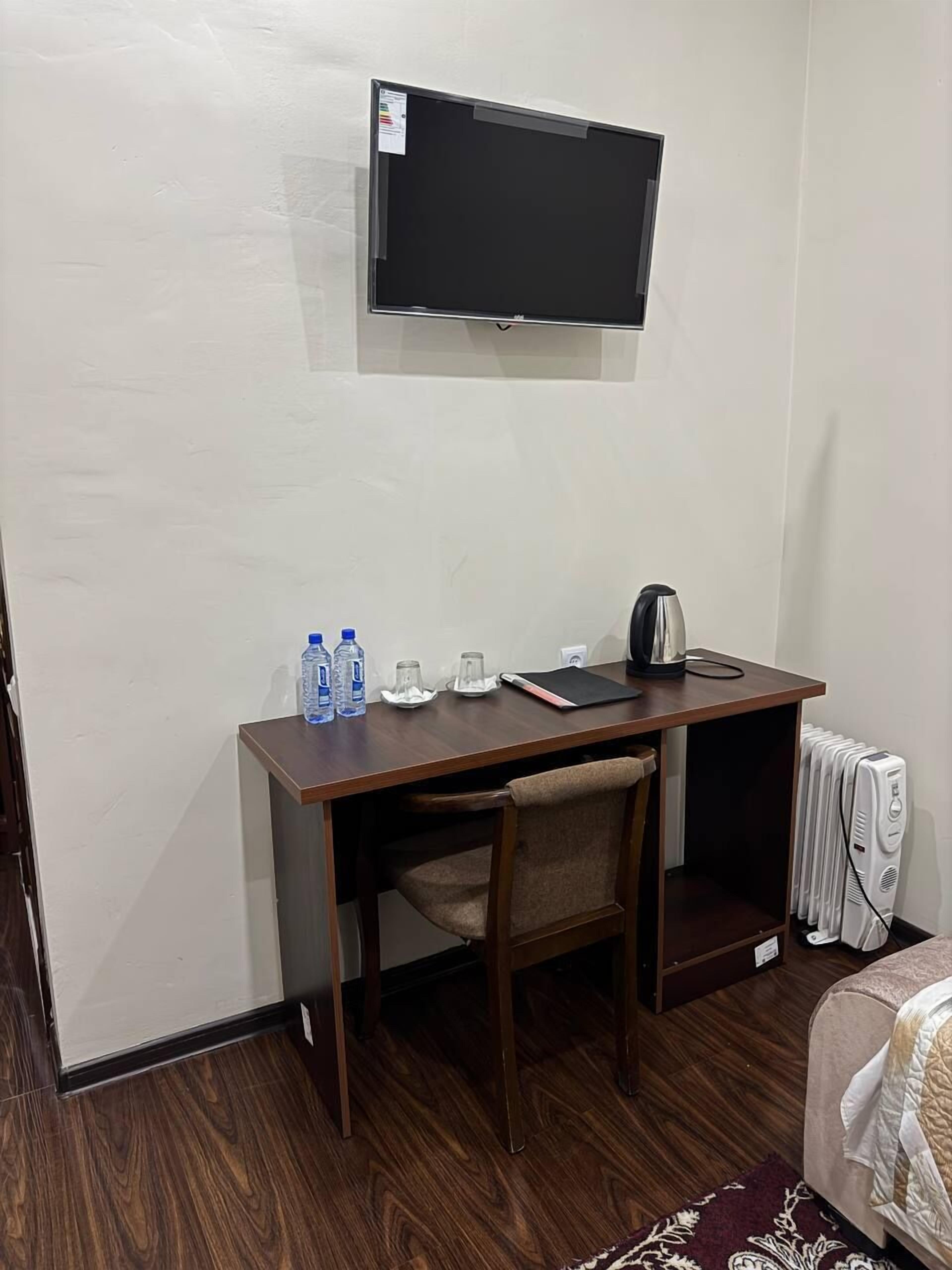 Camera d'albergo con una scrivania in legno, una TV a schermo piatto, un bollitore e un termosifone.
