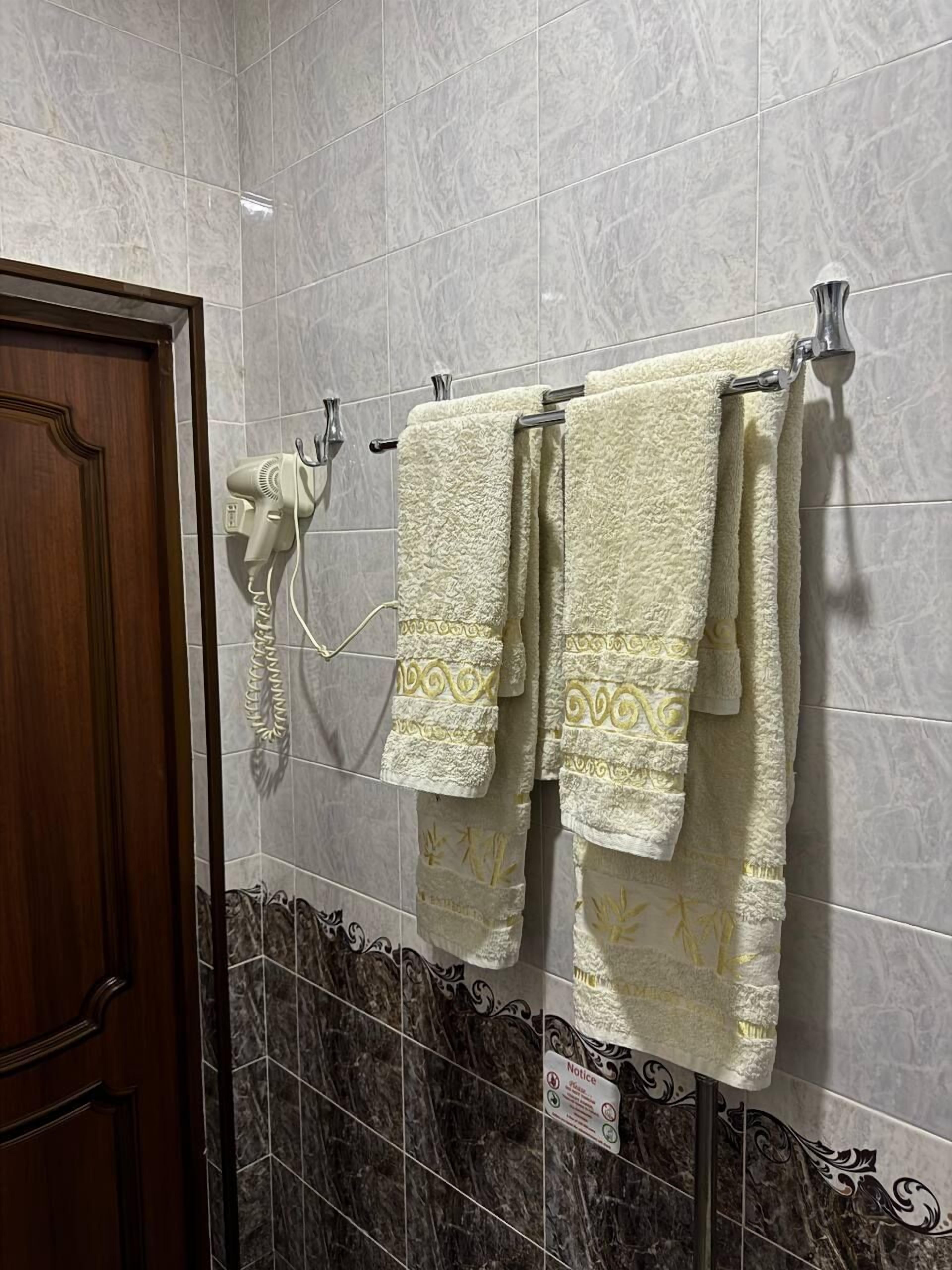 Un baño con baldosas de mármol gris, un secador de pelo montado en la pared y dos toallas colgadas en un tendedero.