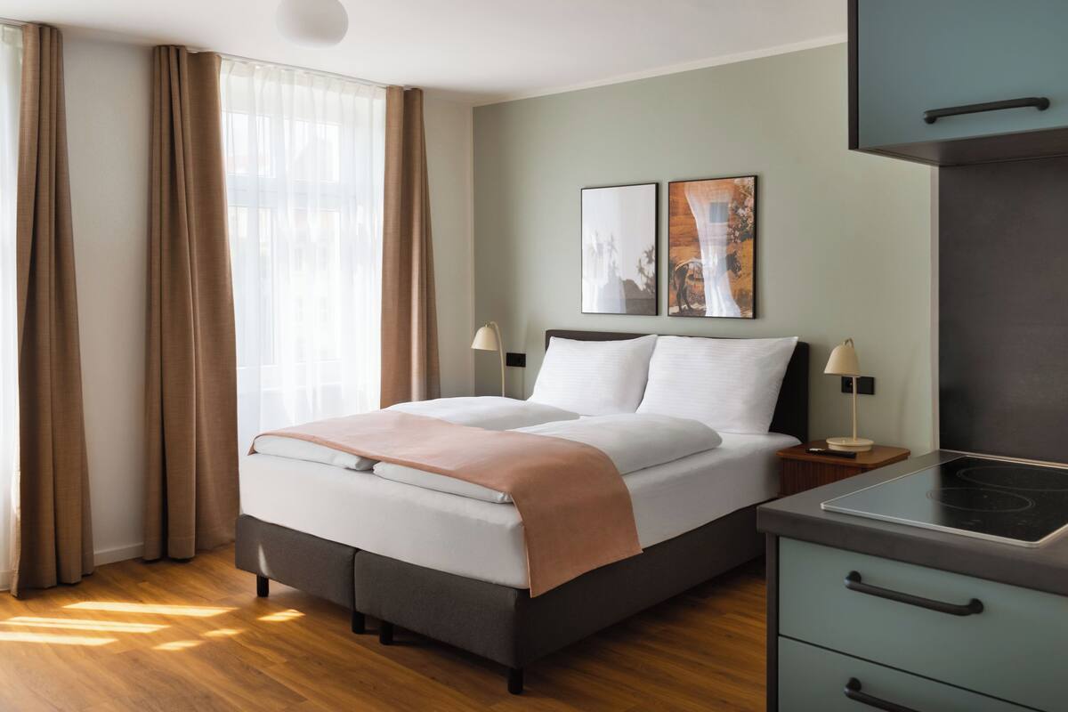 Una habitación de hotel moderna con cama, mesitas de noche, escritorio y estufa integrada.