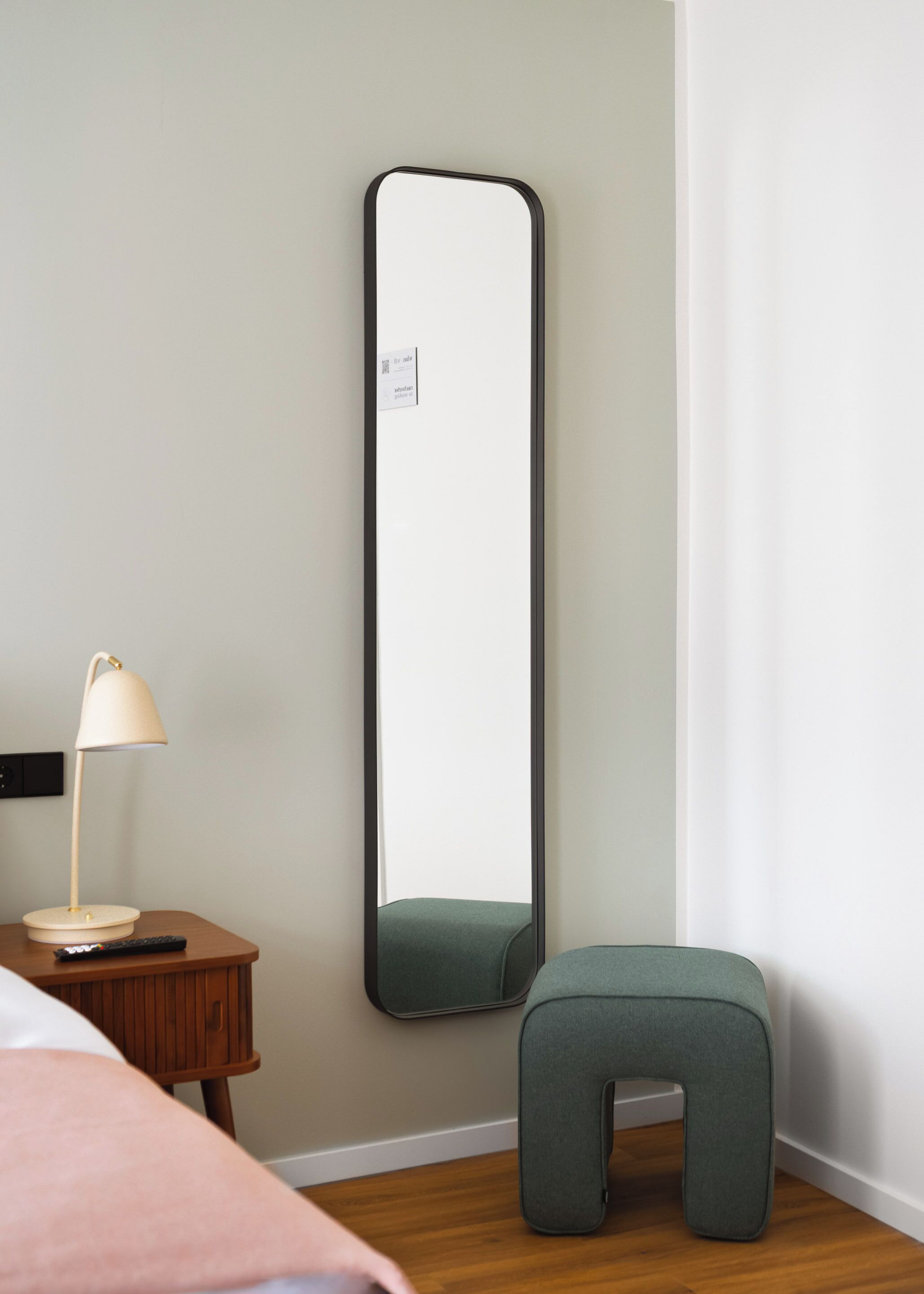 Ein Zimmer mit einem großen Spiegel, einem Nachttisch mit Lampe und einem grünen Hocker.