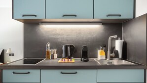 Cozinha moderna com armários azul-claros, bancada preta e eletrodomésticos de aço inoxidável, incluindo chaleira, máquina de café e torradeira.