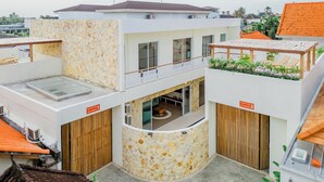 A modern multi-level building with a stone facade, a balcony with plants, and a rooftop terrace.