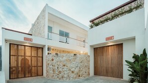 A modern villa with two large wooden doors, a stone wall, and a balcony.