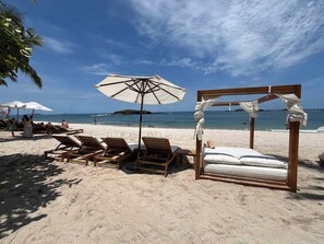 A beachside hotel with wooden lounge chairs, a canopy umbrella, and a wooden bed structure.