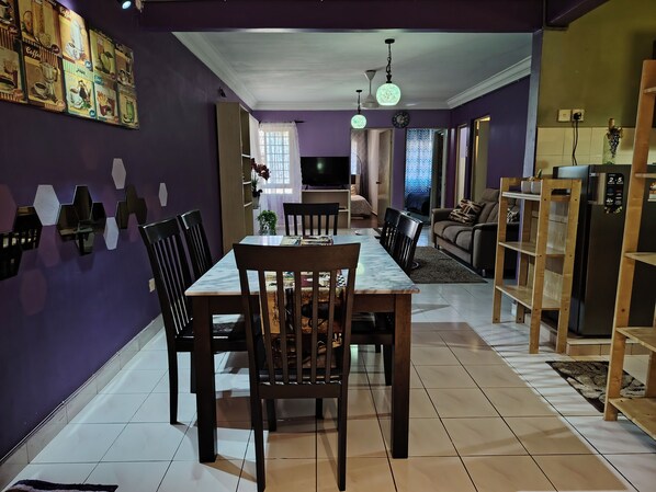 A dining area with a marble table and chairs, a sofa, and a TV in the background.