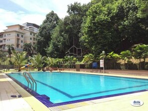 A swimming pool with clear blue water, surrounded by palm trees and a building in the background.