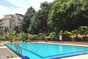 A swimming pool with clear blue water, surrounded by palm trees and a building in the background. - Cosy Home in Damansara (Sungai Buloh)