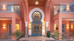 A hotel entrance with a central archway, two balconies, and a tiled courtyard.