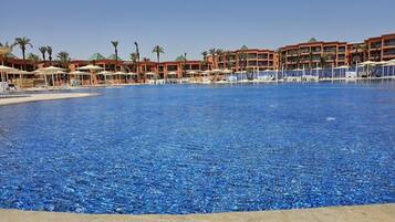 Une grande piscine à l’eau d’un bleu limpide, entourée de palmiers et bordée d’un hôtel doté de nombreux balcons.