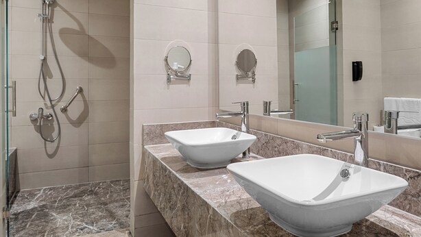 Un baño moderno con dos lavamanos sobre encimera, ducha con cerramiento de vidrio y un espejo grande.