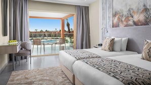 A hotel room with a large bed, a desk with a chair, a view of a pool and palm trees.