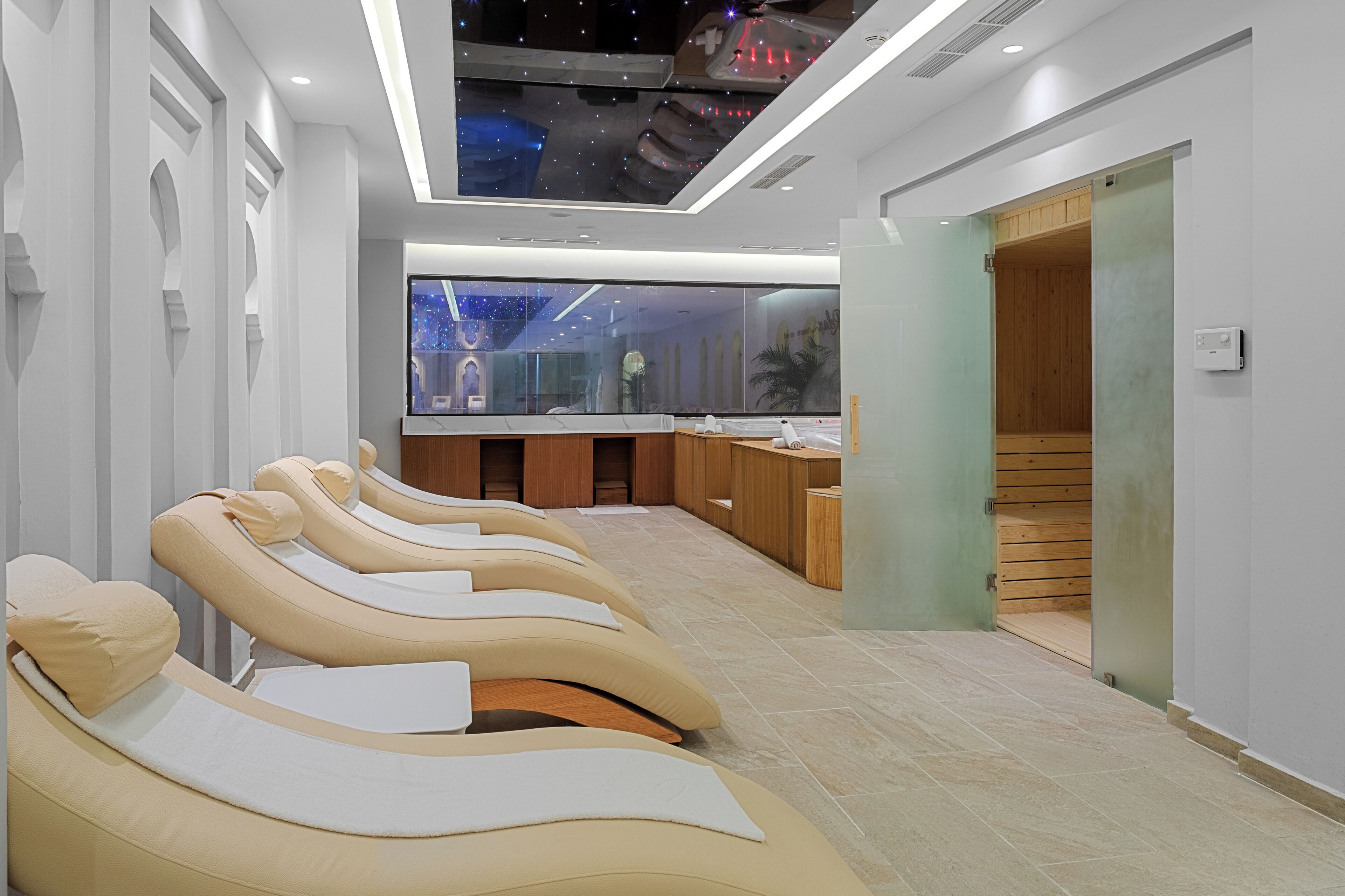 Un espace de bien-être moderne doté de fauteuils de massage, d’un comptoir d’accueil et d’une grande fenêtre offrant une vue sur un ciel étoilé.