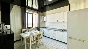 A modern kitchen with white cabinets, a dining table with chairs, and a window with curtains. - Golden house (Tashkent)