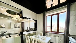 A modern kitchen with a dining area, featuring a large window with a city view, a built-in microwave, and a hanging light fixture. - Golden house (Tashkent)
