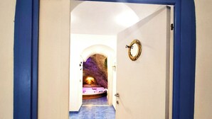 Un couloir mène à une pièce où se trouvent un lit, un miroir et une porte dotée d’une poignée ronde.
