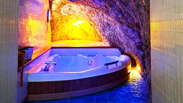 Un espace de bien-être avec un jacuzzi, aménagé dans un décor rappelant une grotte et éclairé de lumières bleues et oranges.