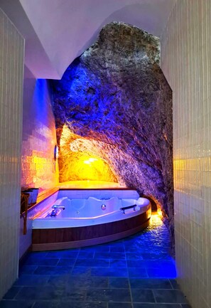 Un espace de bien-être avec un jacuzzi, aménagé dans un décor rappelant une grotte et éclairé de lumières bleues et oranges.