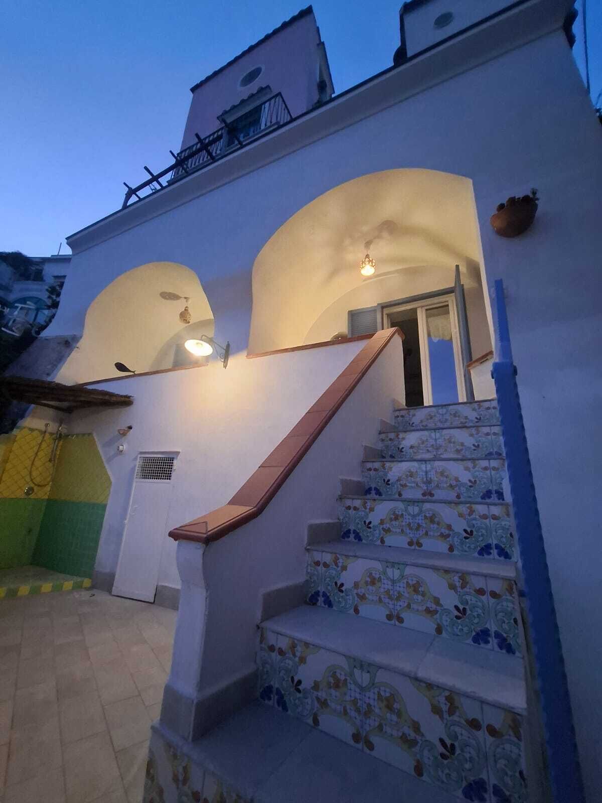 A staircase with colorful tiles leading to a door, a small balcony, and a light fixture above.