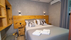 A neatly arranged bedroom with a large bed, two bedside tables, a wooden headboard, a small bedside table with a lamp, a wall-mounted air conditioner, and a wooden wardrobe. - Bom pra Cachorro (Morro de São Paulo)