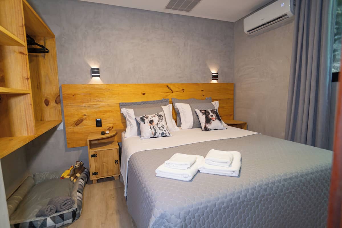 A neatly arranged bedroom with a large bed, two bedside tables, a wooden headboard, a small bedside table with a lamp, a wall-mounted air conditioner, and a wooden wardrobe.