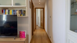 Un pasillo con suelo de madera, un televisor sobre un mueble y estanterías llenas de libros.
