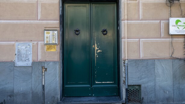 Puertas verdes dobles con un adorno metálico en la parte superior, una pequeña ventana debajo y un cartel en la pared a la izquierda.