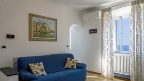 Un sofá azul con cojines estampados, un cuadro en la pared y una ventana con cortinas.