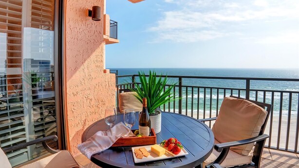 A balcony with a table set for two, featuring a bottle of wine, strawberries, cheese, and crackers.