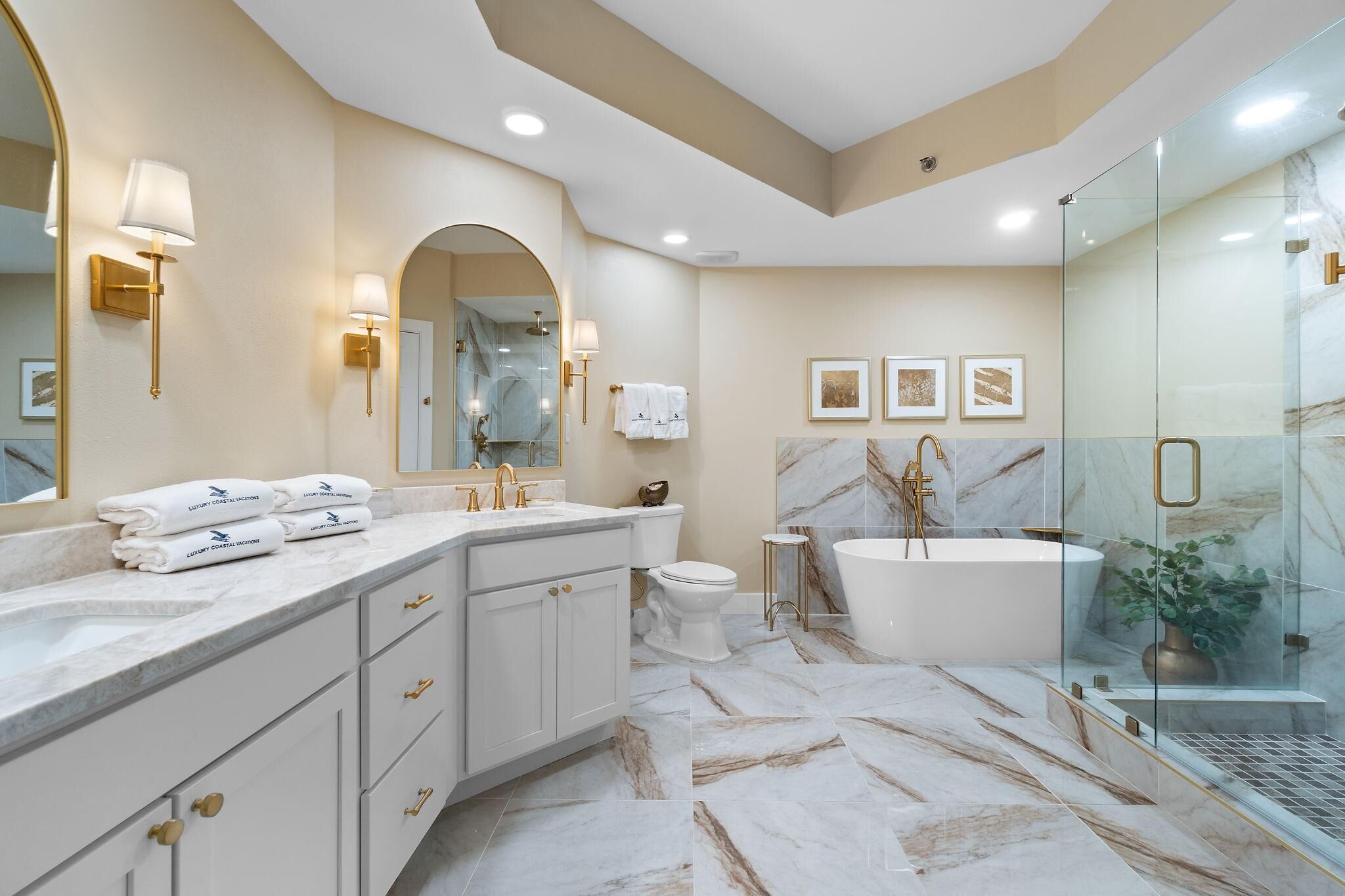 Une salle de bain moderne avec un sol en marbre, une baignoire sur pieds, une douche à parois de verre et un meuble-lavabo avec des accessoires dorés.