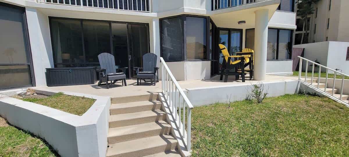 Un edificio moderno con un área de estar cubierta al aire libre, una escalera que conduce a la entrada y un pequeño jardín.