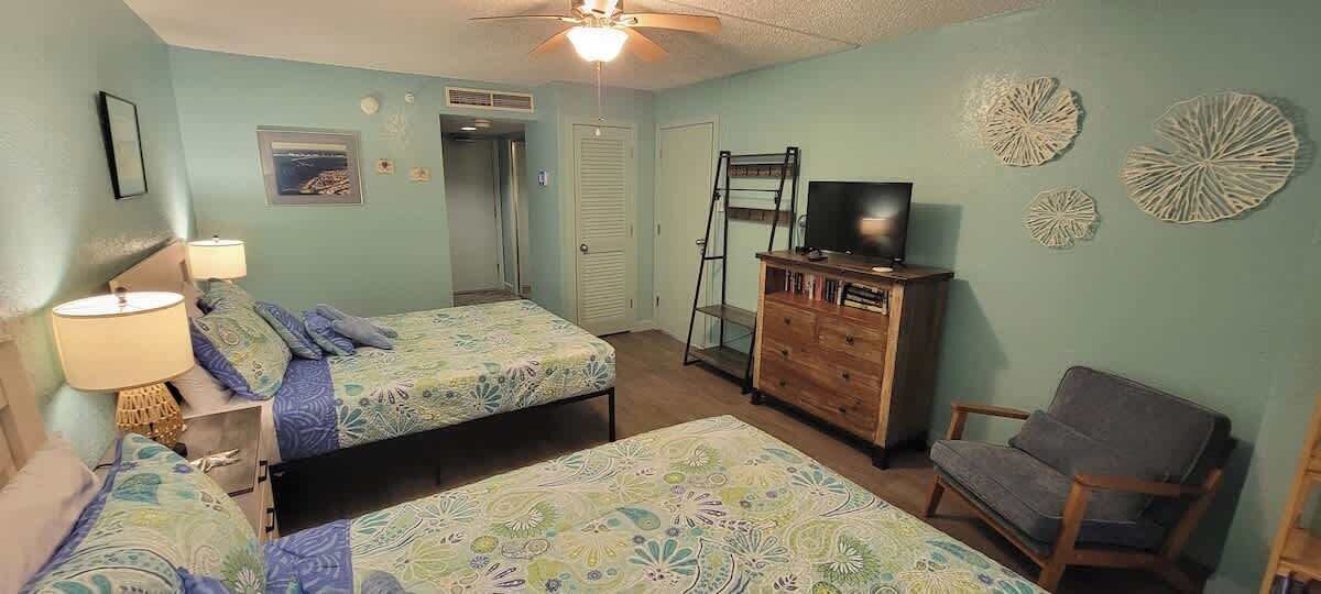 A bedroom with two beds, a dresser, a chair, a TV, and decorative wall art.
