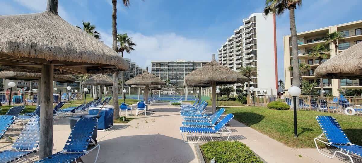 Ein Resort mit Poolbereich, blauen Liegestühlen und Reetdachschirmen.