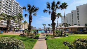 A hotel courtyard with a swimming pool, palm trees, and a pathway leading to the pool. - Beachfront Hotspot - New Furnishings - Pool - 1st Floor (South Padre Island)
