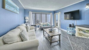 A living room with a sofa, a coffee table, a TV, and a window with curtains.
