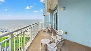 A balcony with a view of the beach, white plastic chairs, and a small table.